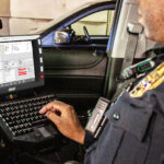 law enforcement officer operating a digitax atomo 10 mobile data terminal with keyboard in a patrol car